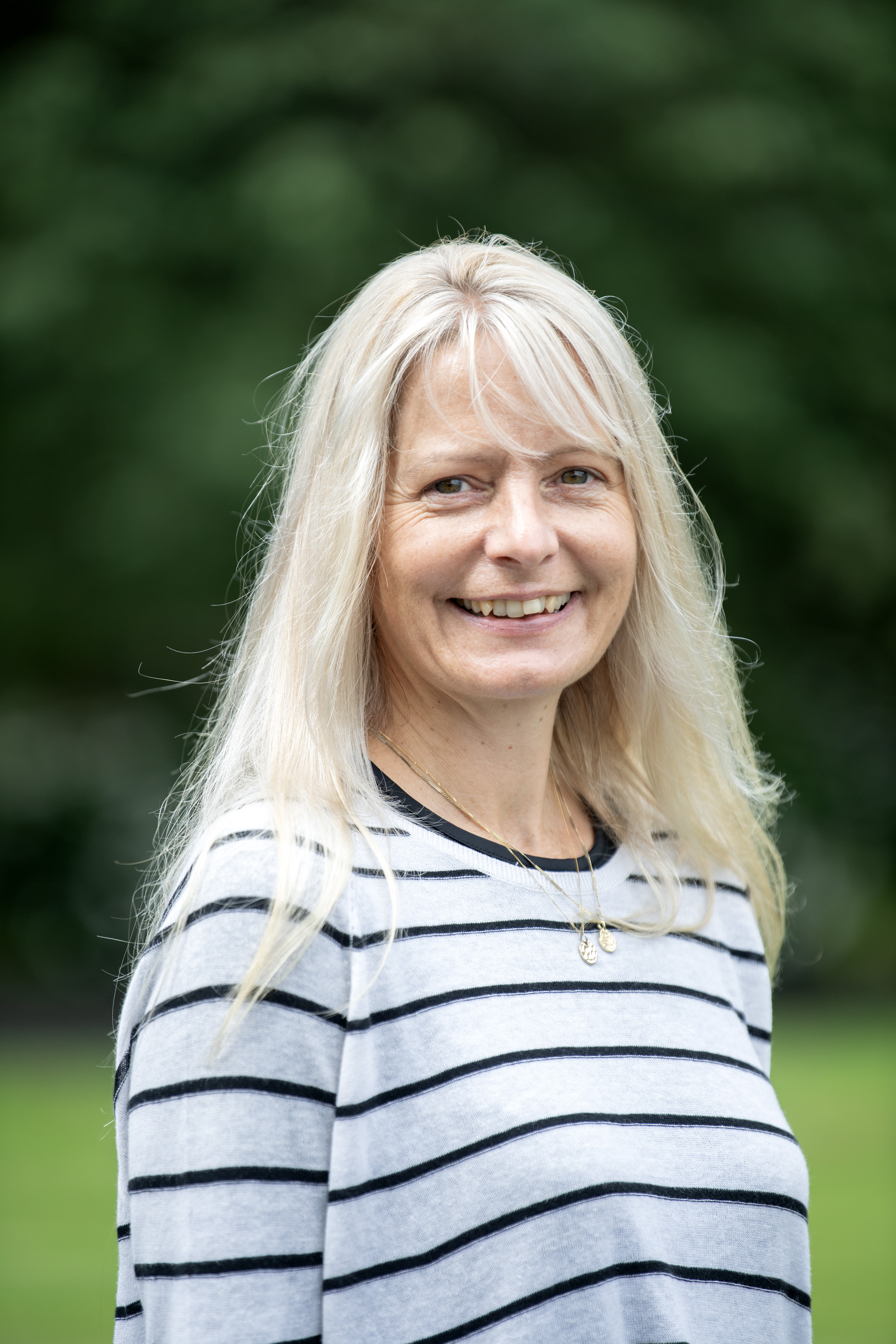 A smiling person with long blond hair is wearing a white and black striped top.