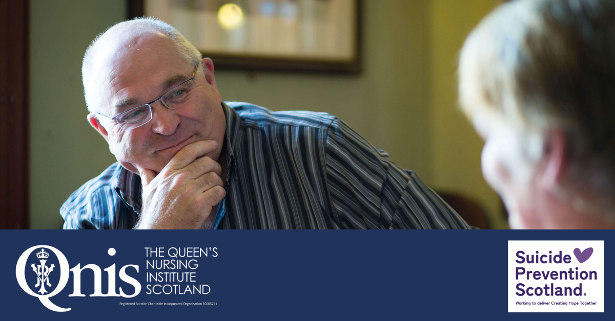 A person with glasses, wearing a striped shirt, sits thoughtfully with their hand resting on their chin, engaged in conversation with another person whose face is partially out of focus in the foreground. The image includes logos for The Queen’s Nursing Institute Scotland (QNIS) and Suicide Prevention Scotland, with the tagline “Working to deliver Creating Hope Together.