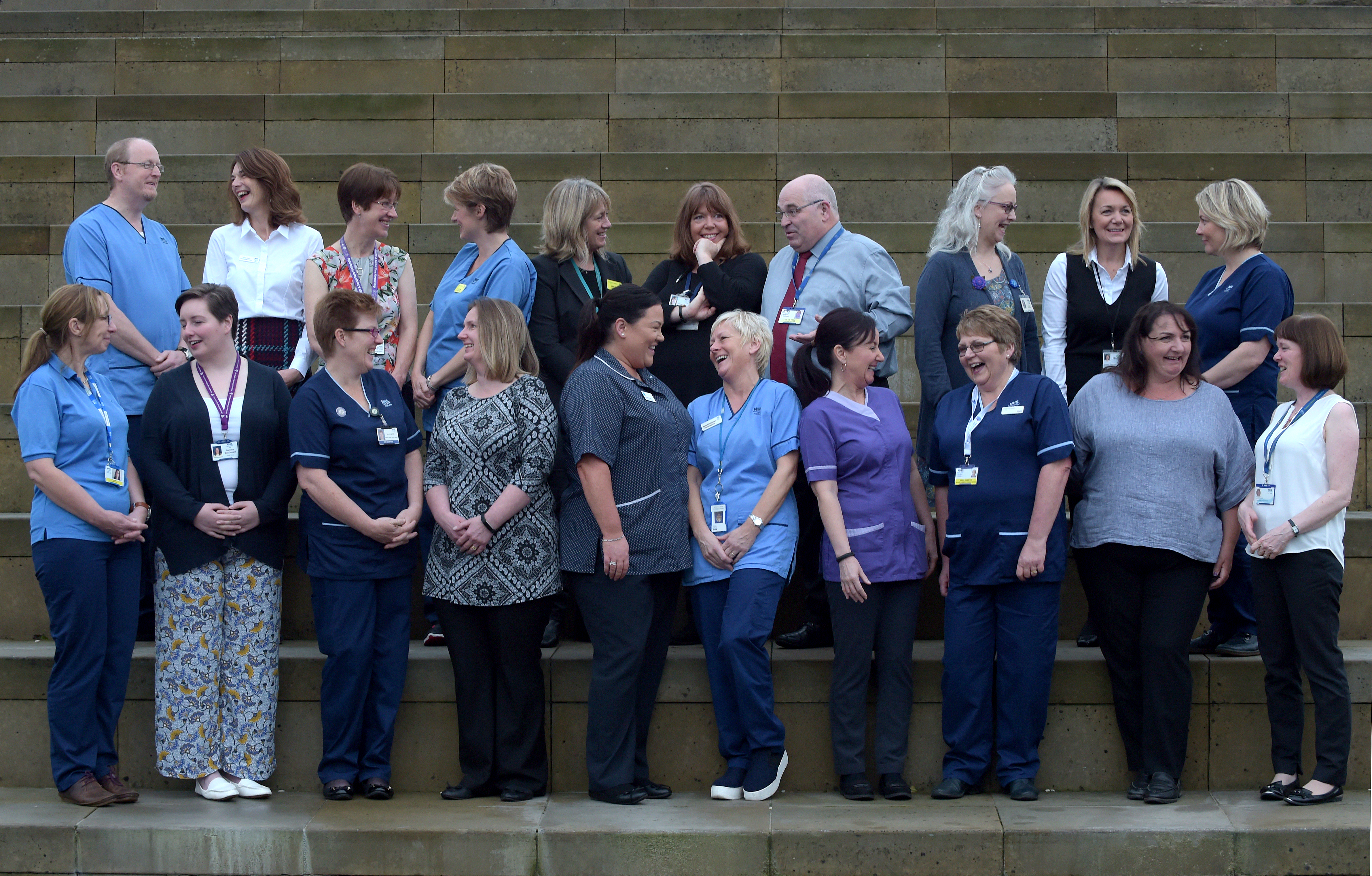 A group of people stand in two rows. They are chatting and smiling.