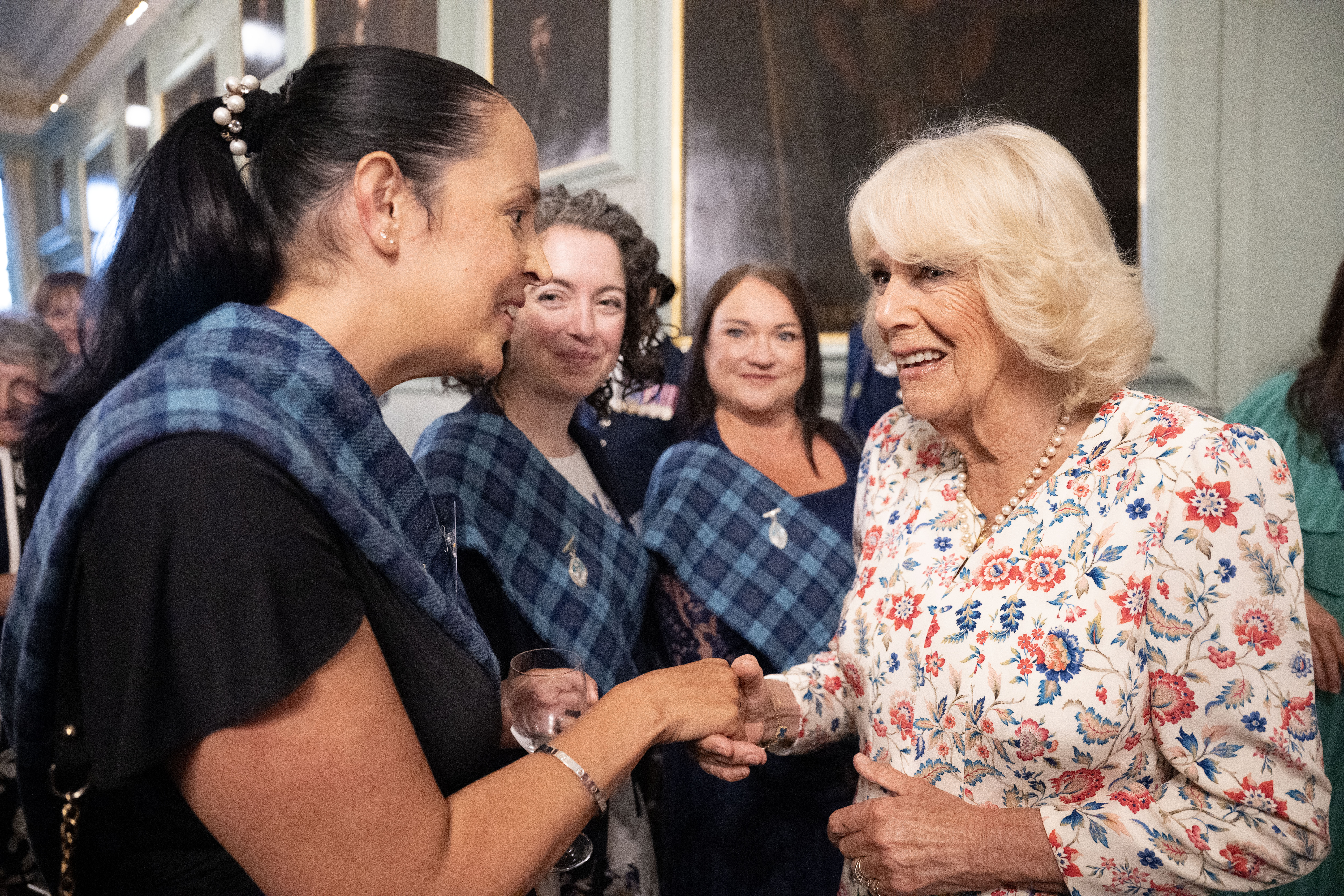 Four people are stood together chatting. Three of the people are wearing tartan sashes. They all look happy.